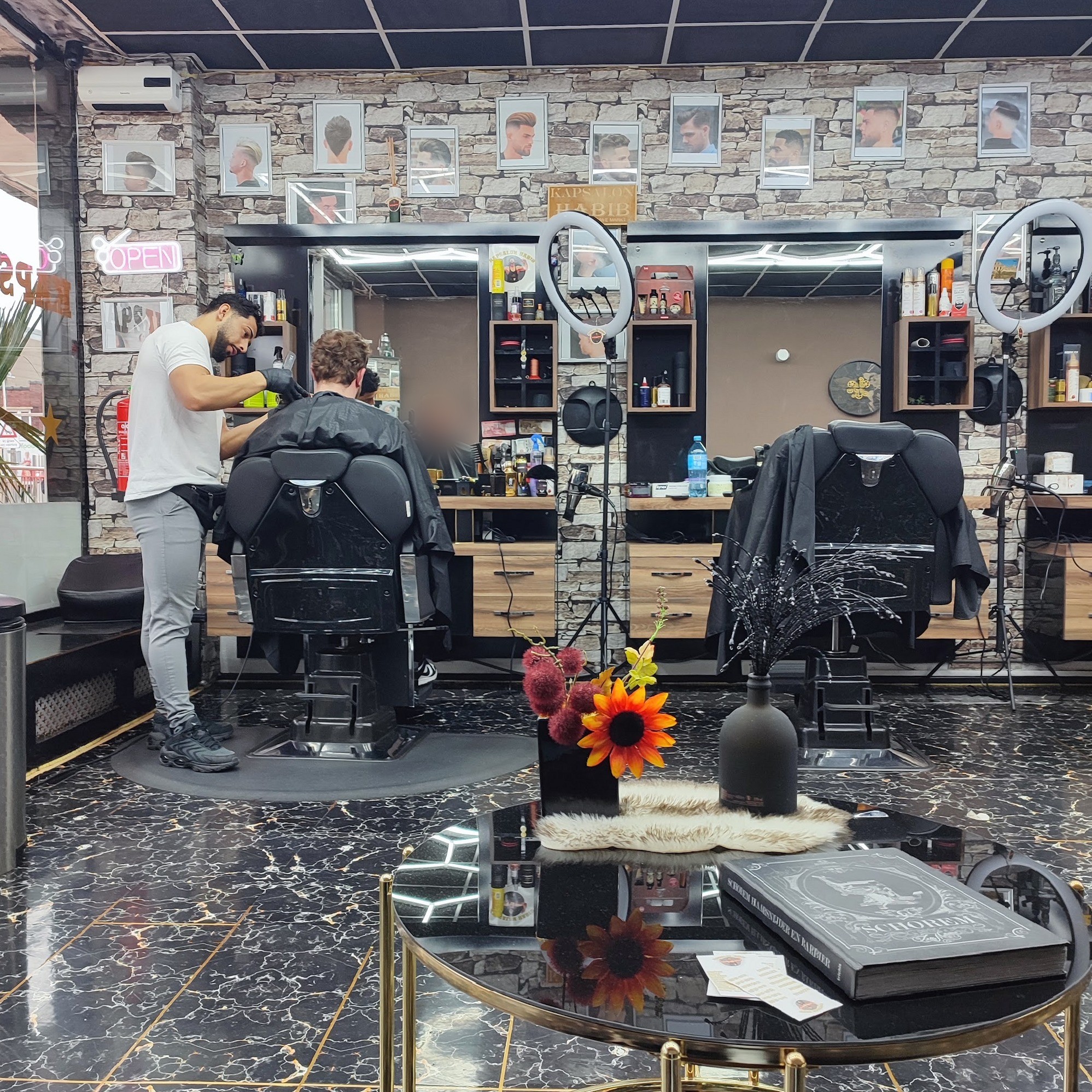 Een kapper aan het werk in Kapsalon Habib, met de zwarte kappersstoelen, ringlampen en de stenen wand