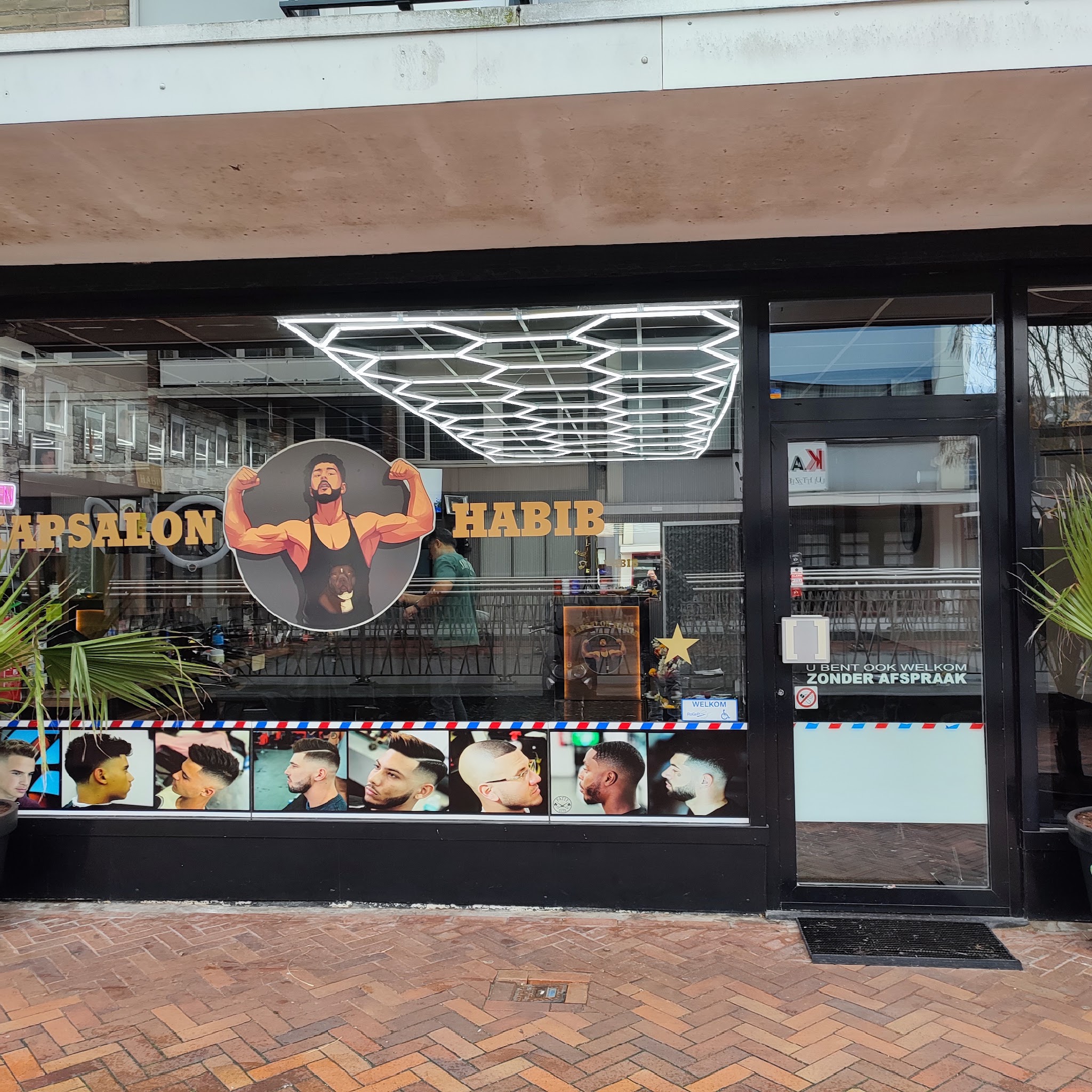 De etalage van Kapsalon Habib met de gouden letters en het logo op het raam